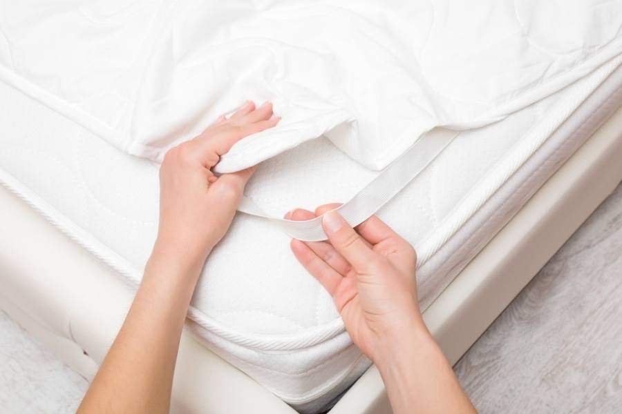 A woman is putting a white cover with an elastic band on the mattress
